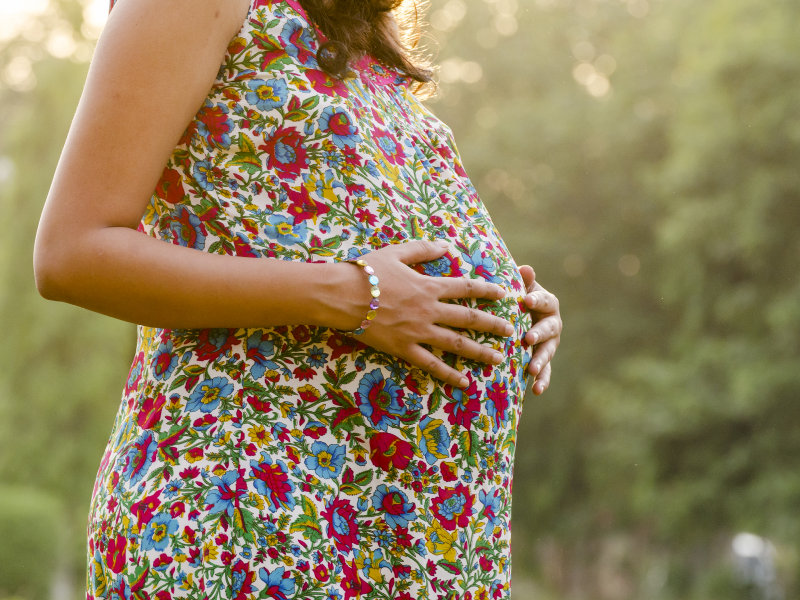 A pregnant woman in a floral dress with her hands on her stomach